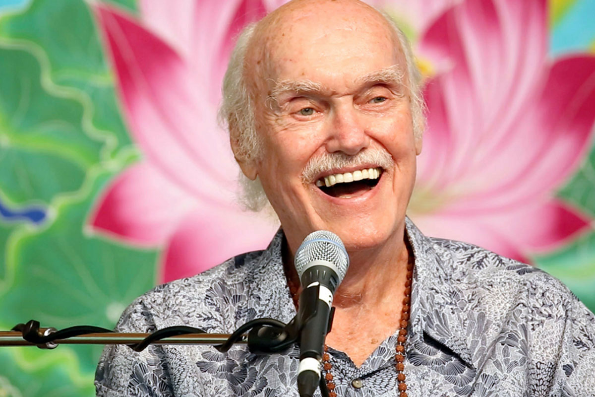 Ram Dass smiling in front of a microphone