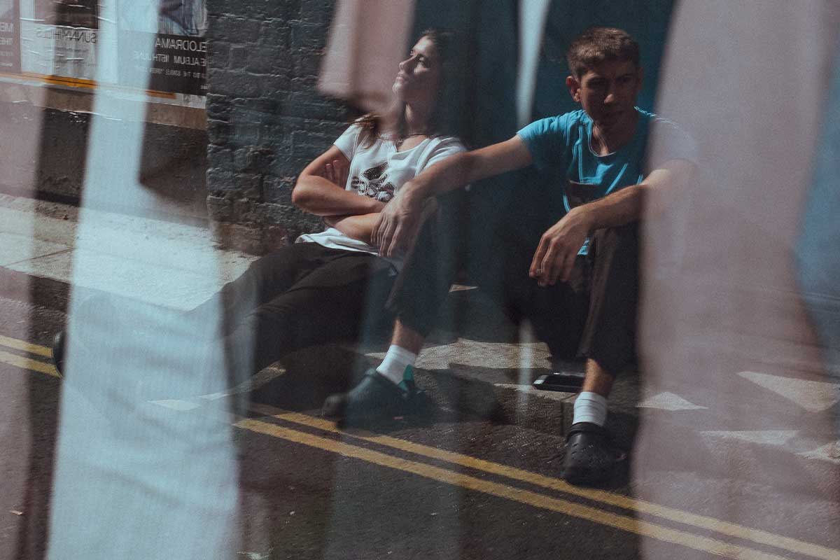two young people sitting on a sidewalk