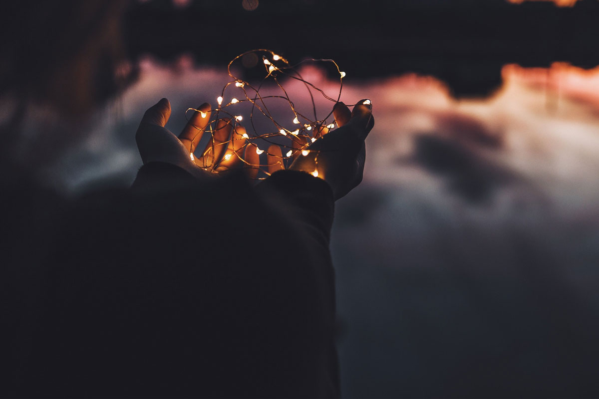 hands holding twinkle lights in front of a sunset