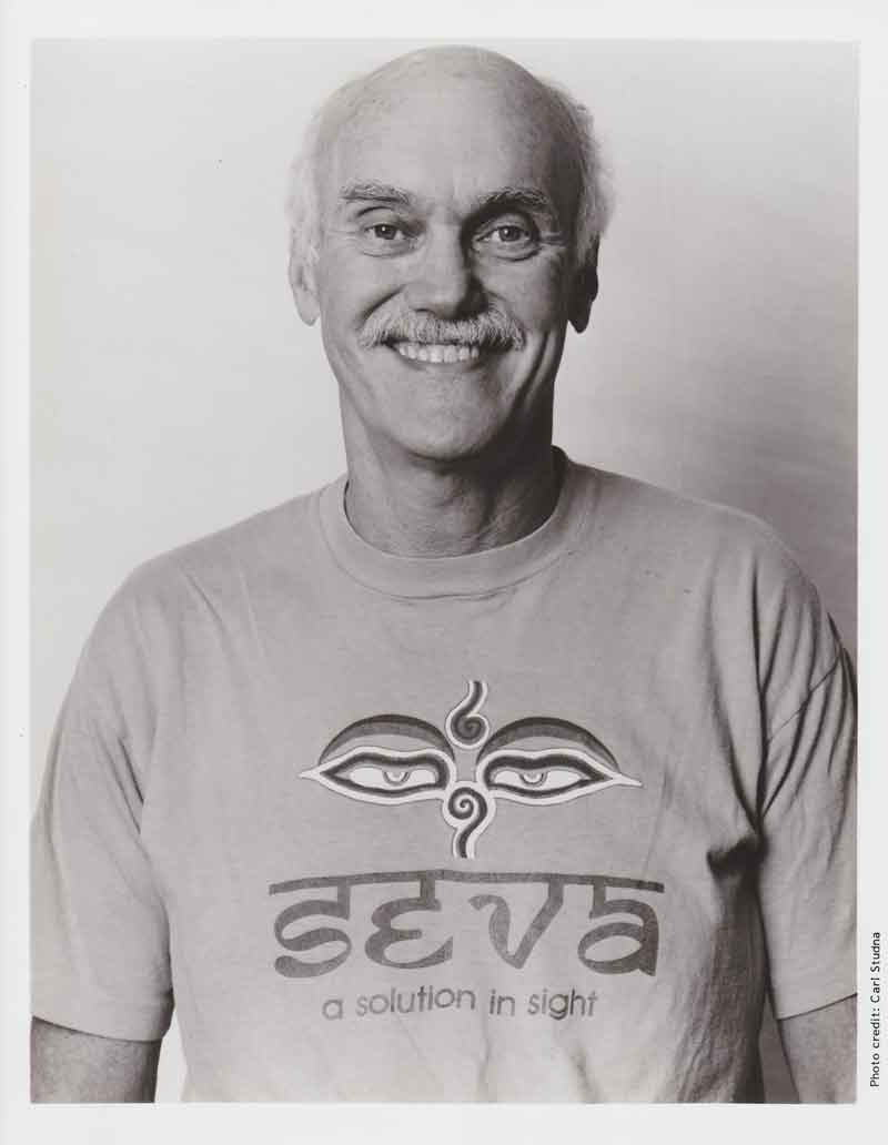 Ram Dass smiling in a Seva shirt